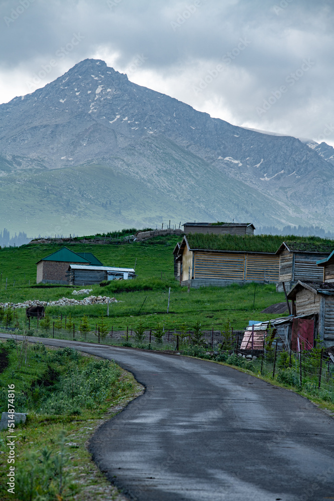 a road to village under mountains in cloudy sky