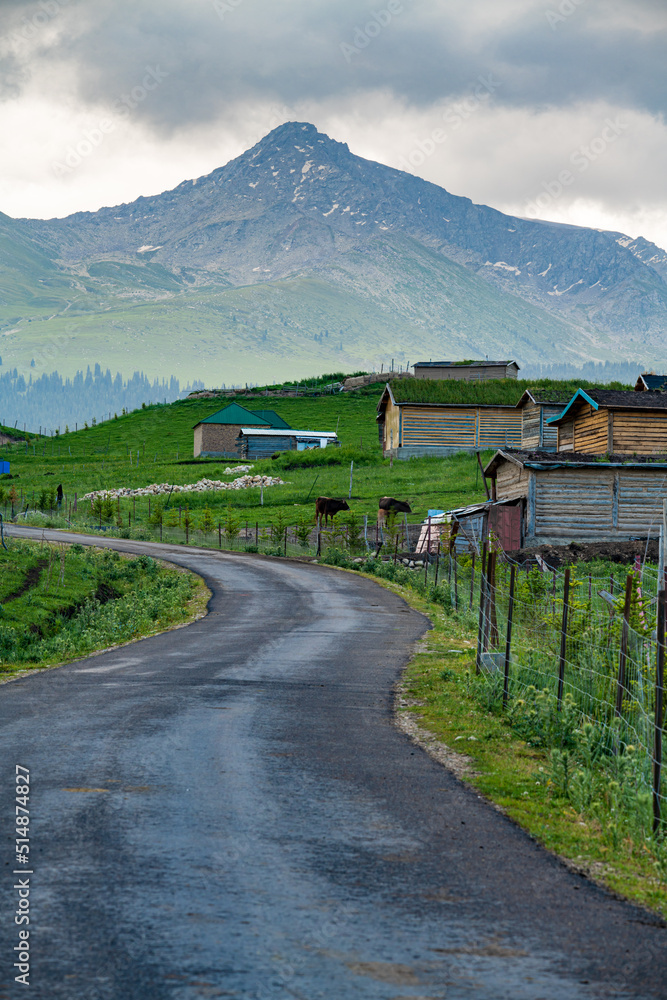 a road to village under mountains in cloudy sky