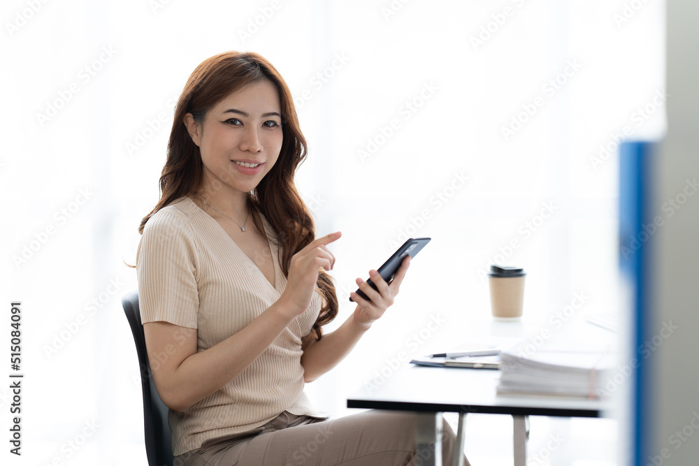 Portrait of smiling young woman with smartphone in her hands, sitting at table in front of laptop. G