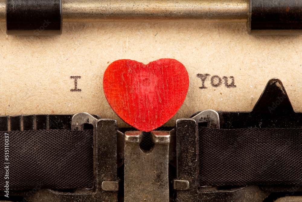 I love you - phrase on typewriter. Valentines Day greetings concept. Little red wooden heart close u