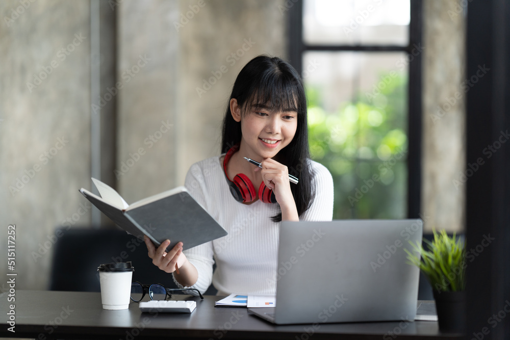 一名年轻的女学生坐在桌子旁，学习时使用电脑笔记本电脑。