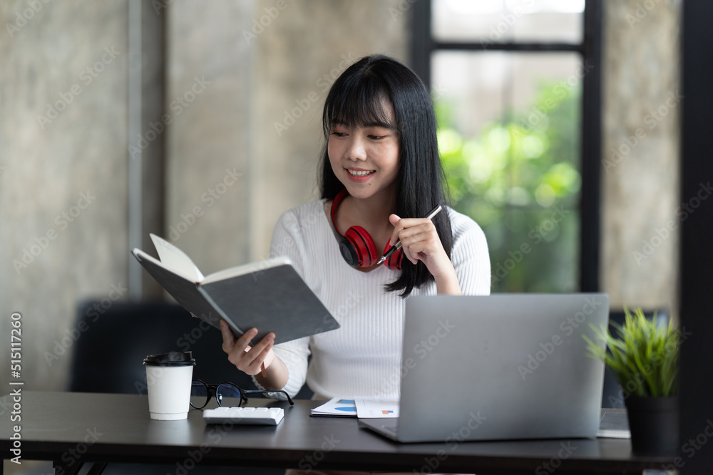 一名年轻的女学生坐在桌子旁，学习时使用电脑笔记本电脑。