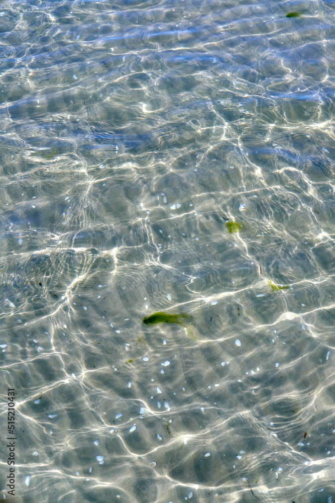 Closeup of shallow waves on a coastline on a sunny day outside. Above view of sunlight reflecting on