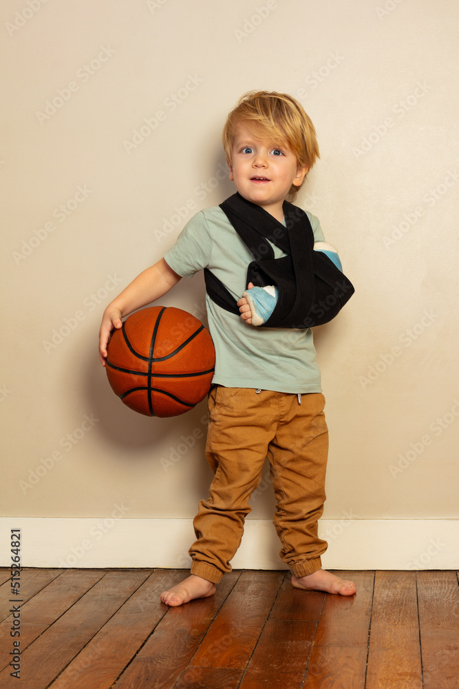 Little blond boy with broken hand holding basketball ball