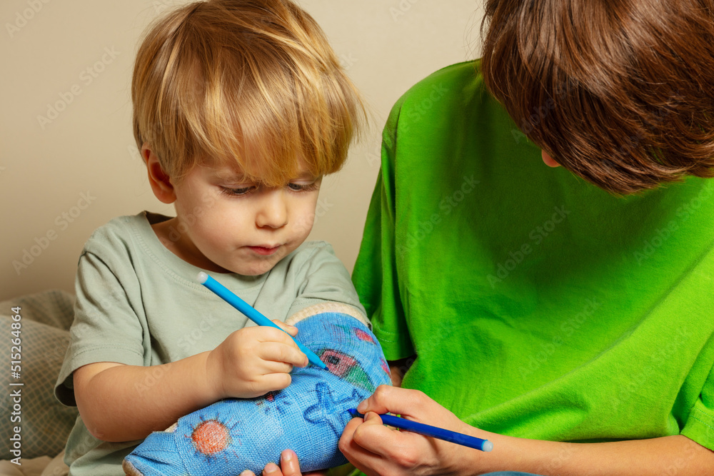 Two kids draw broken hand plaster cast with childish drawings