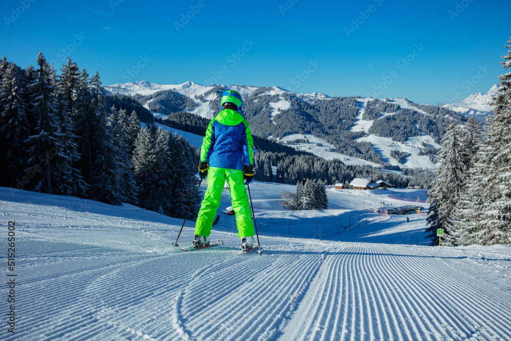 Back view of a boy alpine ski downhill on the fresh track