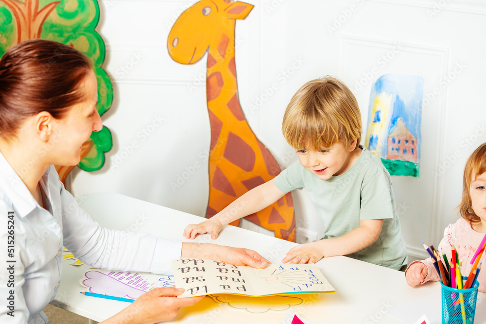 Adult teaches little kids to read letters in the book