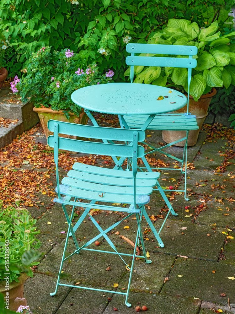 Blue courtyard metal chairs and table in serene, peaceful, lush, private backyard at home on a summe