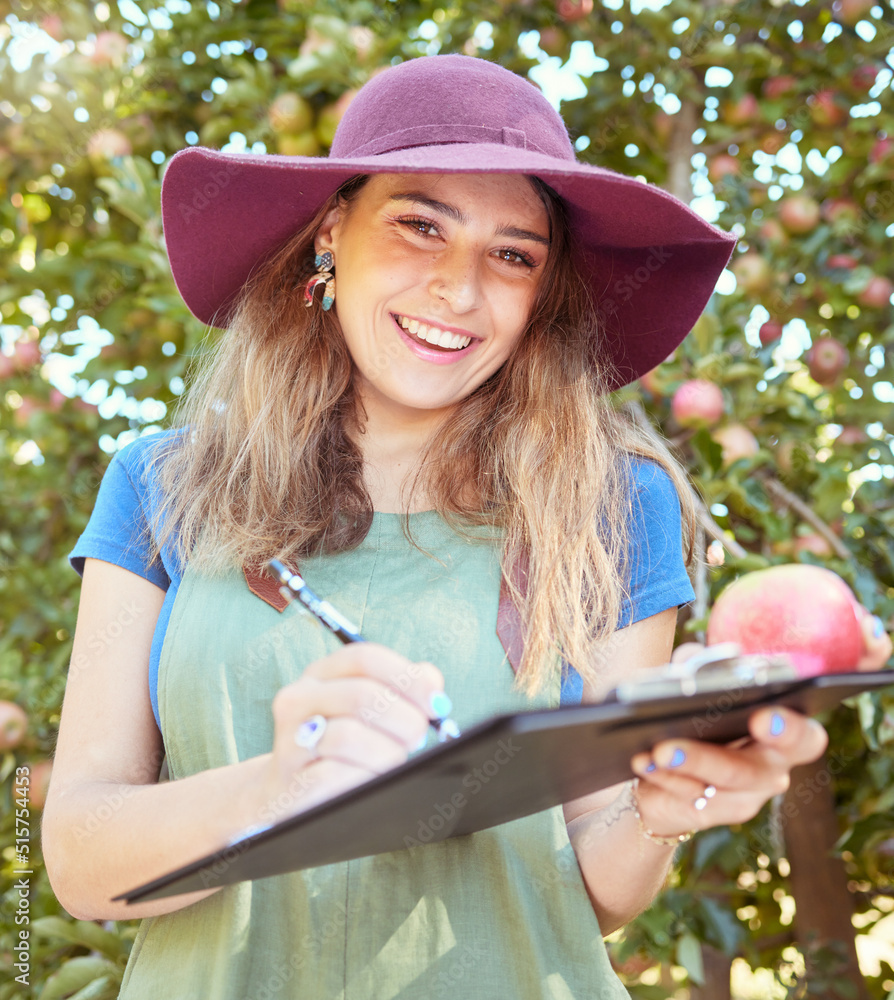 Portrait of female farm worker holding an apple while writing and making notes on a orchard farm dur