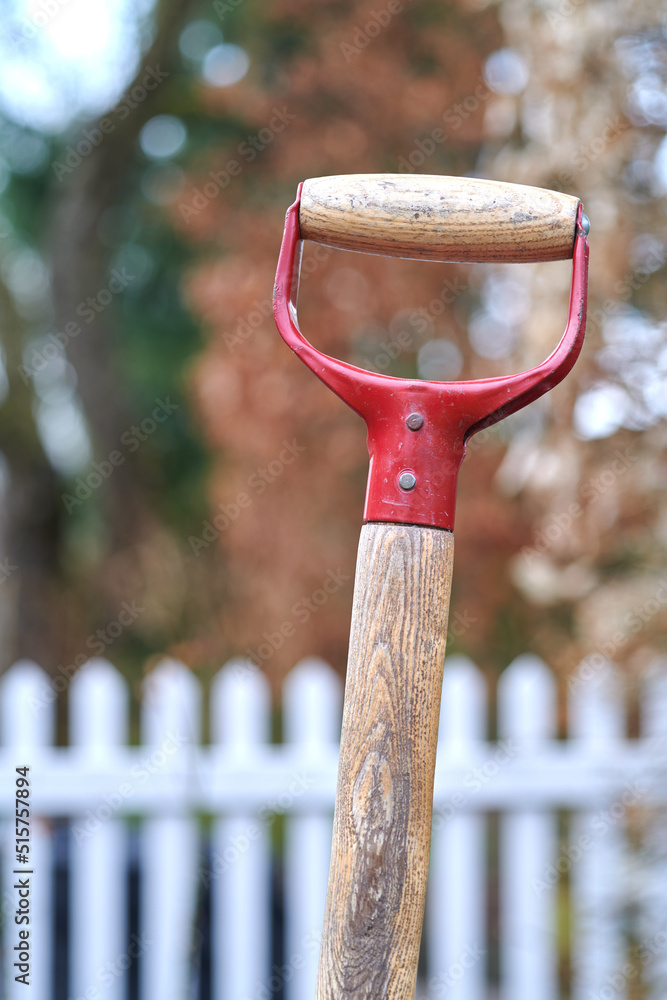 Closeup of a shovel handle in a garden outside against a blur background. Red gardening tool or equi