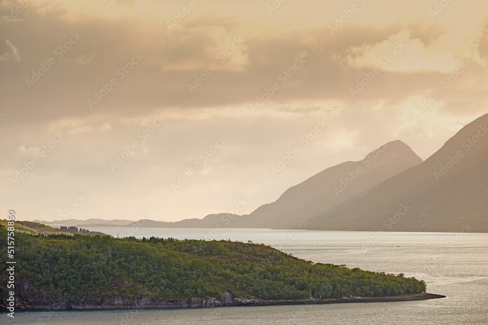 Green hills by the seaside with a sunset sky in Norway. Wild vibrant landscape in Nordland. Calm sea