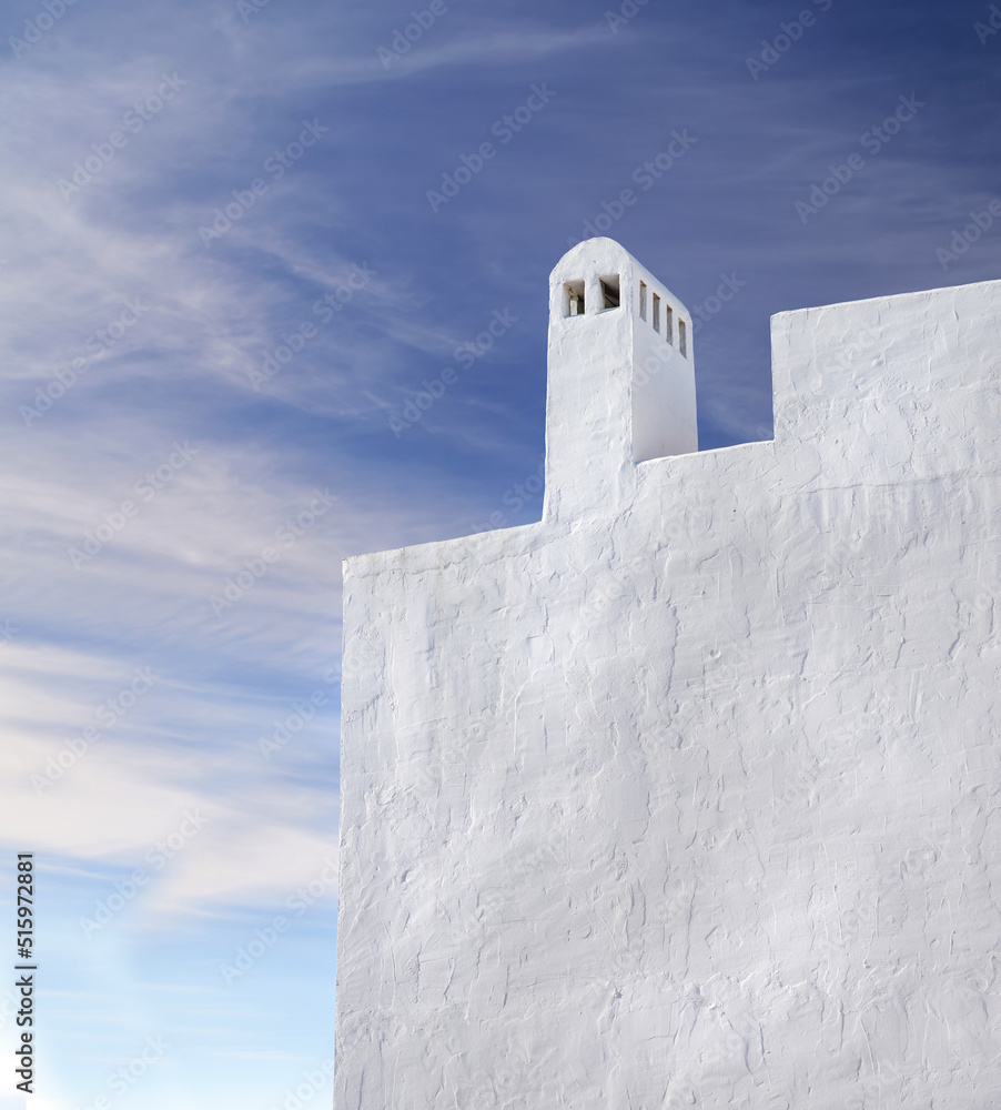 Chimney or bell tower designed on the roof of a white building outside against a cloudy blue sky bac