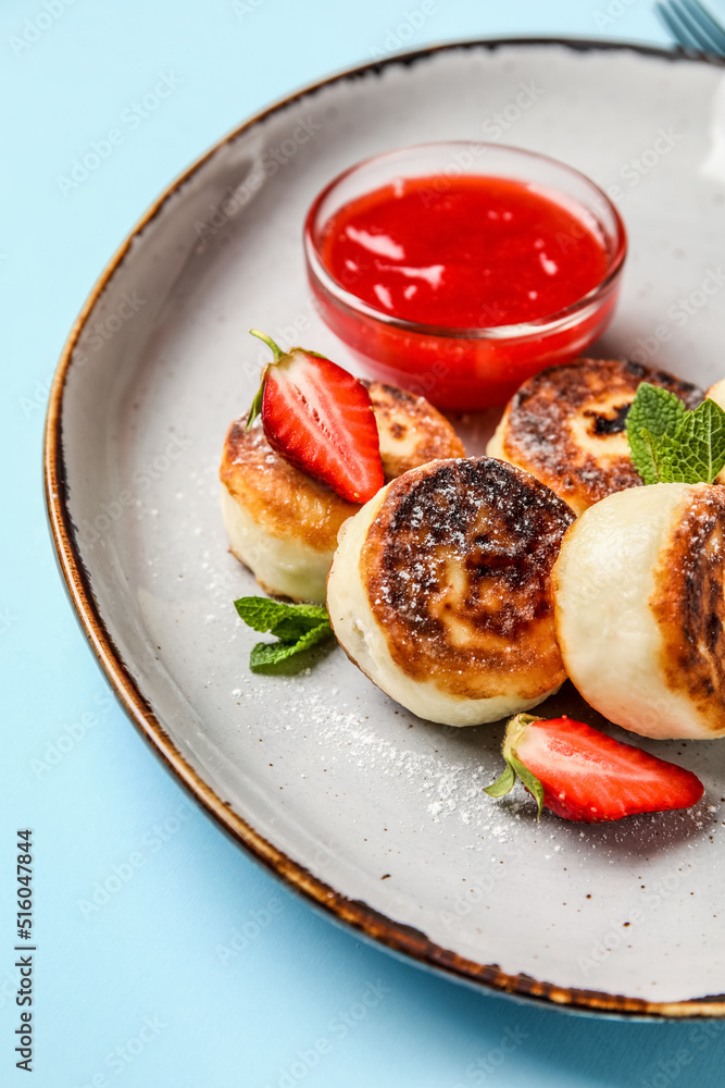 Plate with cottage cheese pancakes and strawberry jam on blue background, closeup