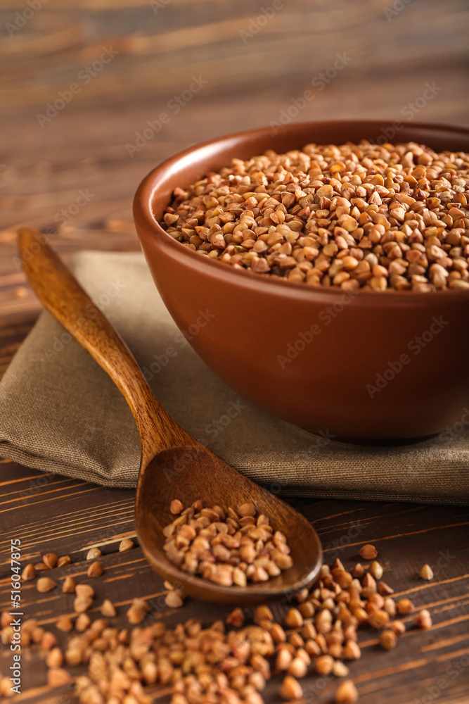 Spoon and bowl with buckwheat grains on wooden background