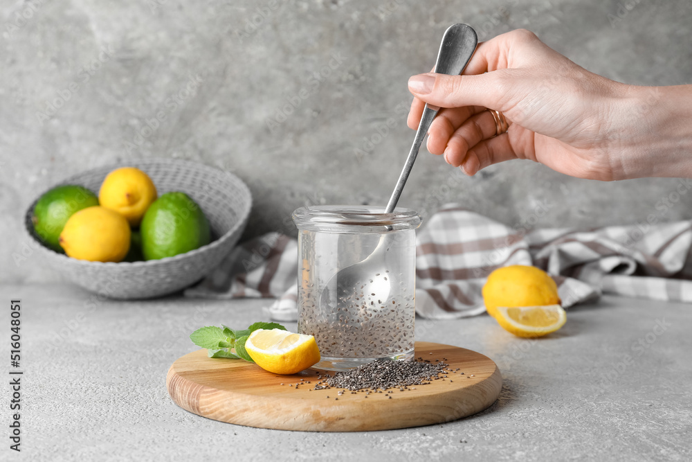 Woman stirring chia seeds in glass of water on grey background