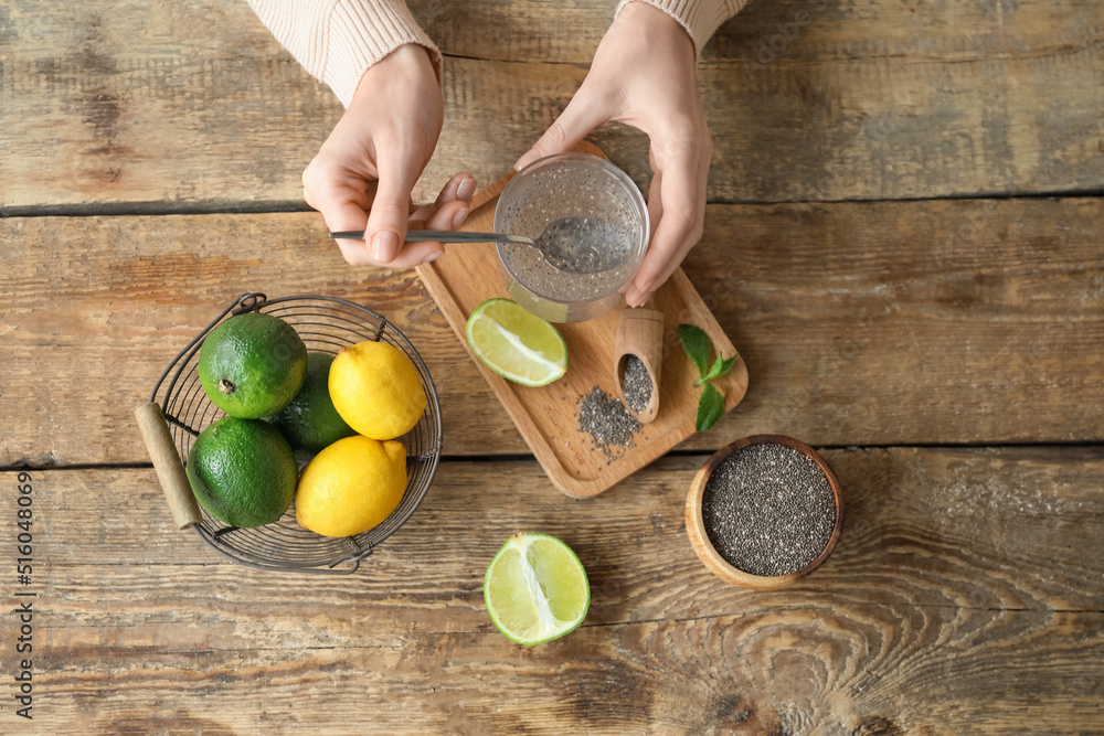 Woman stirring chia seeds in glass of water on wooden table with citrus fruits