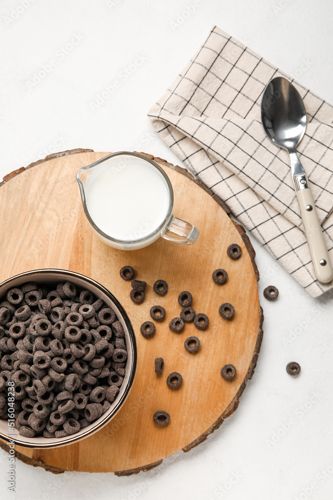 Wooden board with bowl of black cereal rings and milk on light background