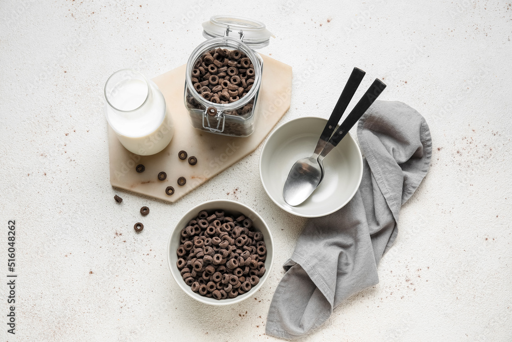 Composition with bowl of black cereal rings and milk on light background