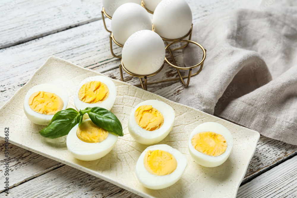 Plate with halves of boiled chicken eggs on light wooden background, closeup