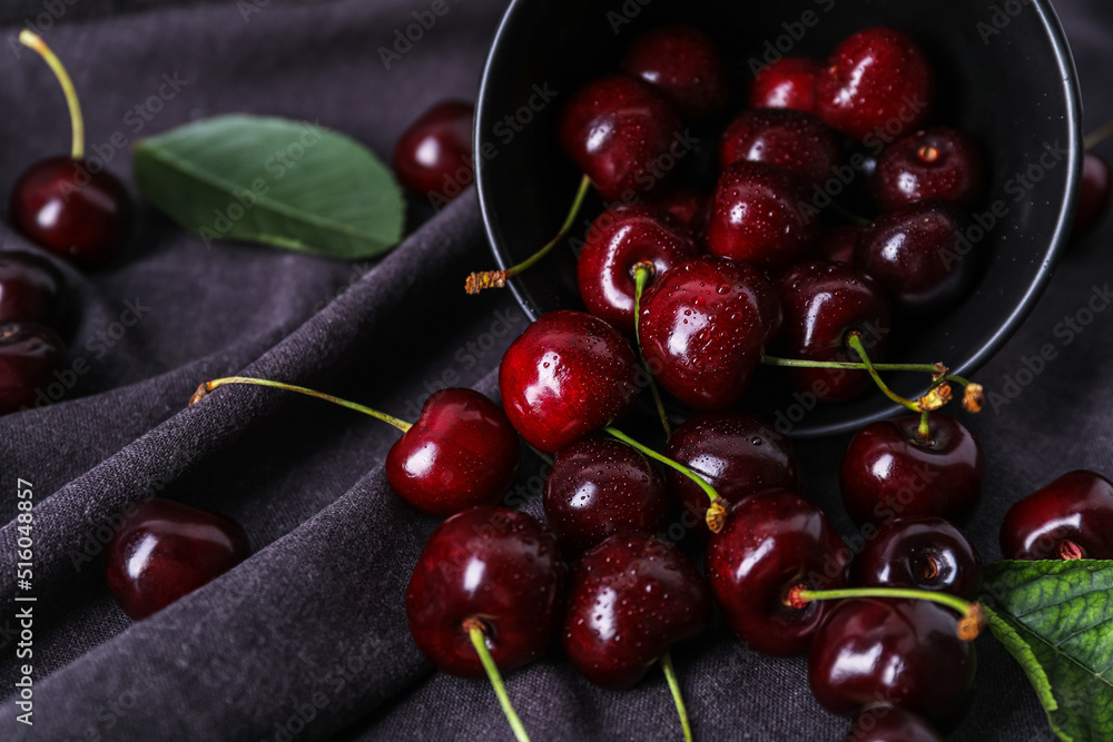 Overturned bowl of ripe cherries on fabric background, closeup