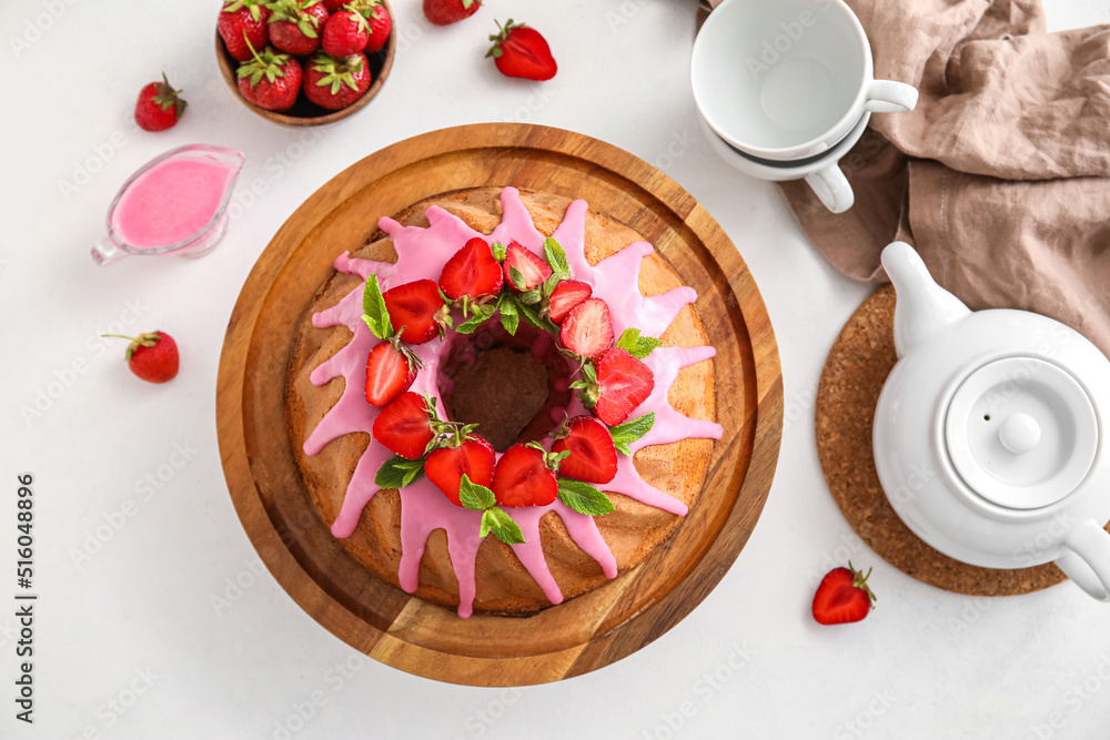 Wooden board with tasty strawberry cake, cups and teapot on light background