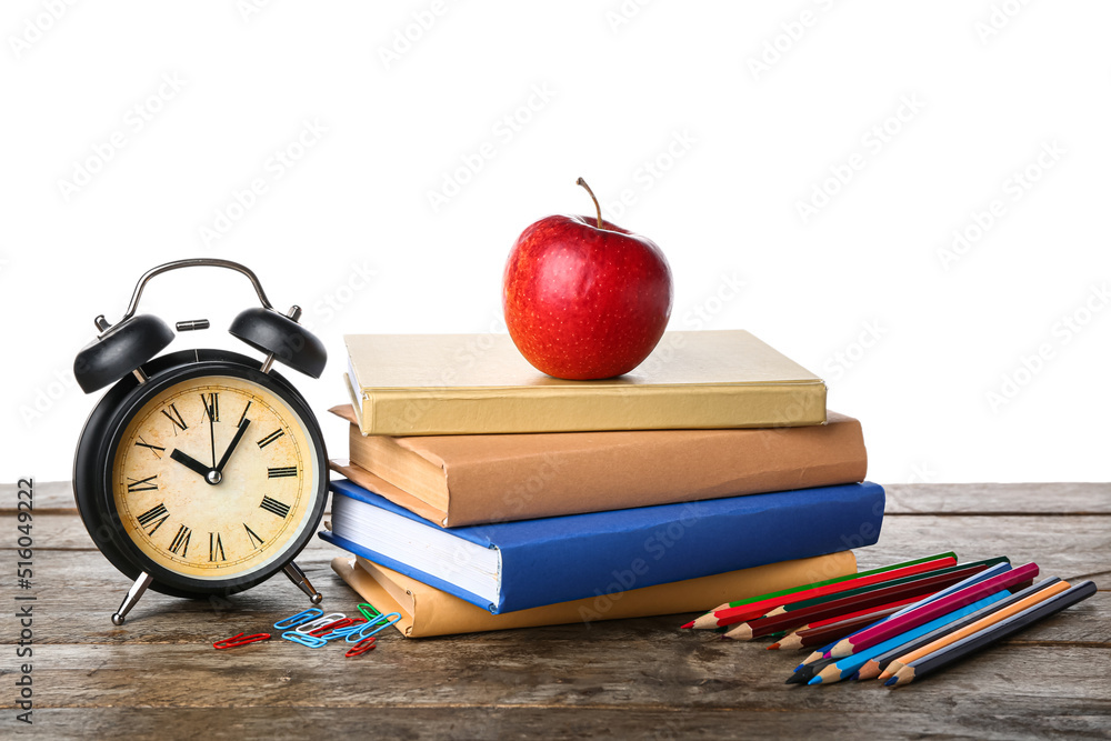 School books with apple, stationery and alarm clock on table against white background