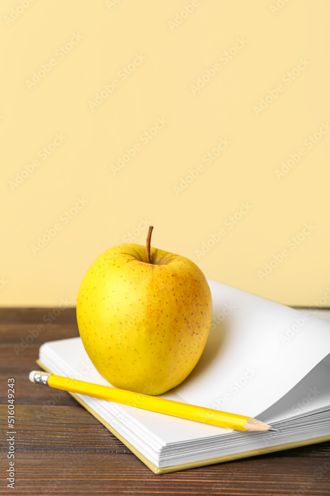 School book with apple and pencil on table against color background