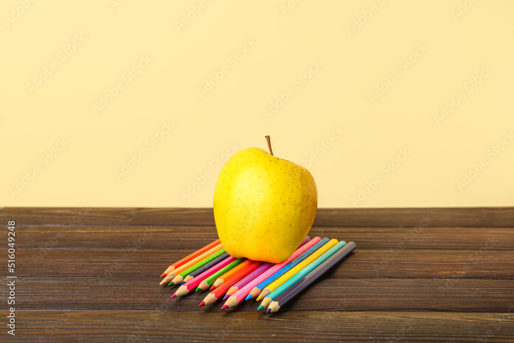 Apple with pencils on table against color background