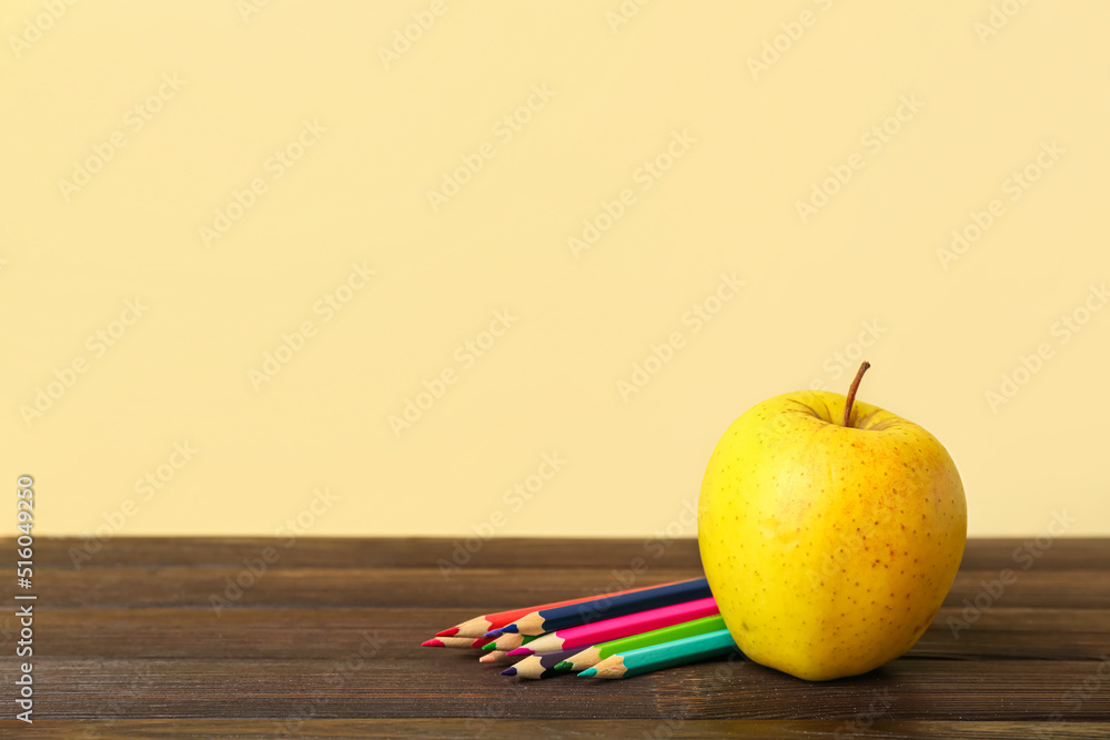 Apple with pencils on table against color background