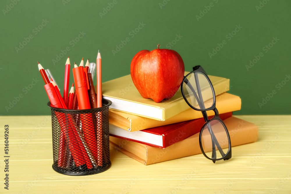 School stationery with apple and eyeglasses on table against green background