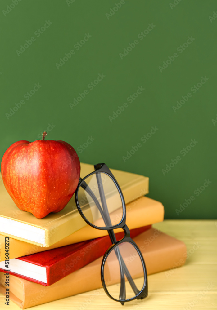 School books with apple and eyeglasses on table against green background