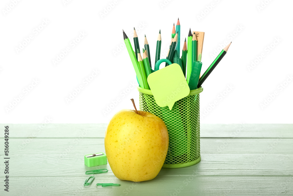 Holder with school stationery and apple on table against white background