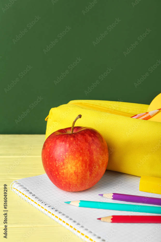 Pencil case with apple and notebook on table against green background