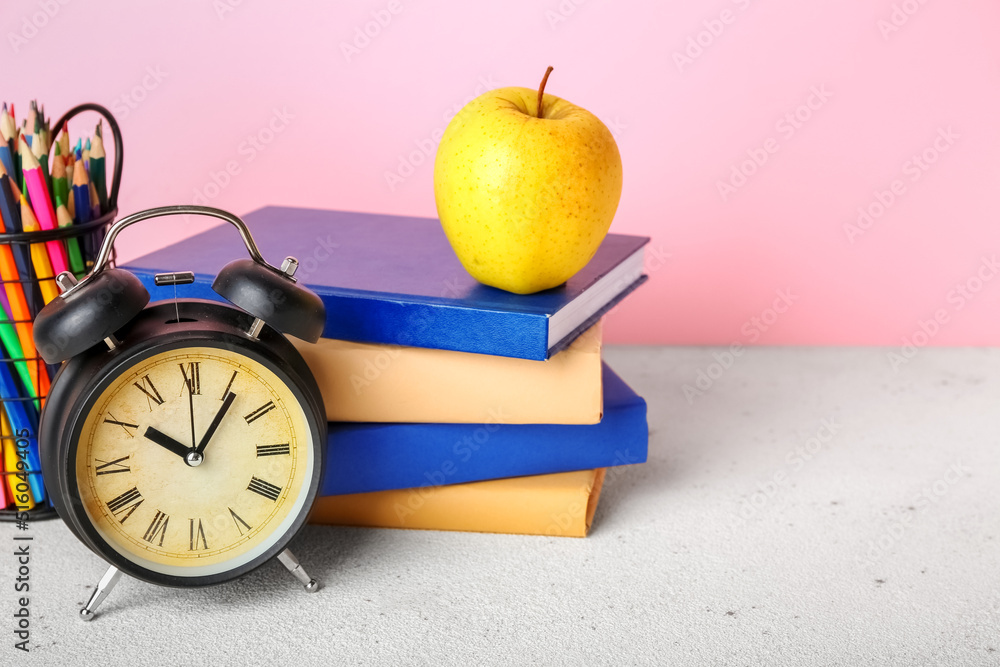 School stationery with apple and alarm clock on table against pink background