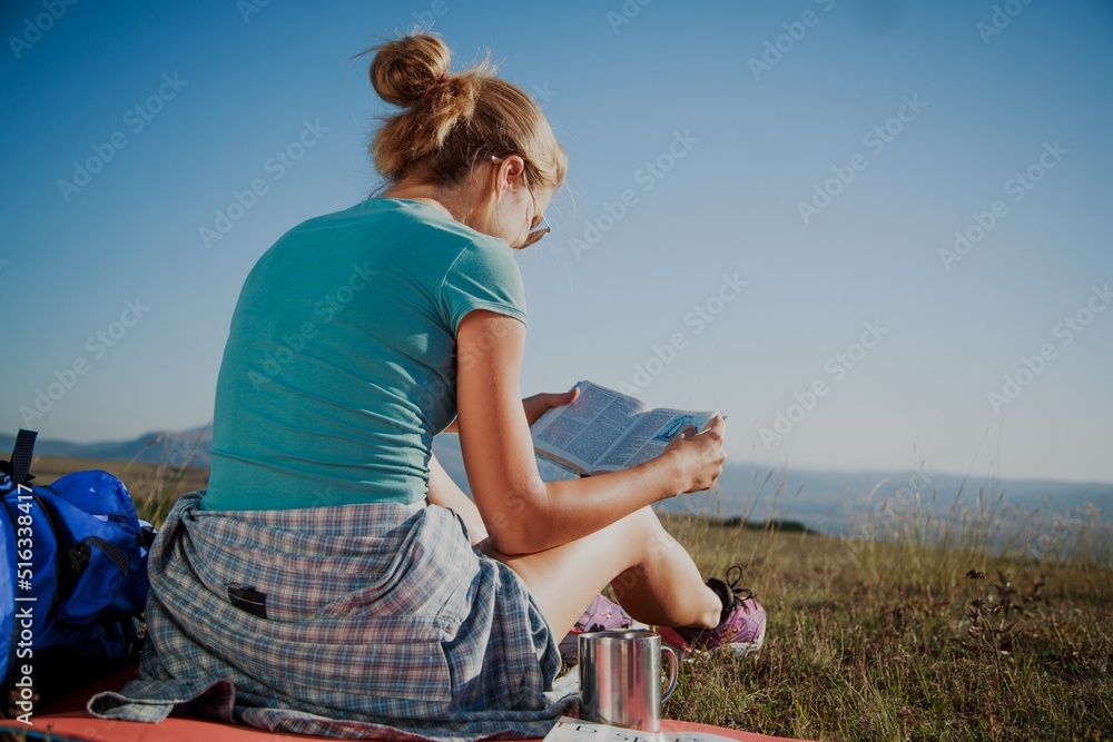 Girl reading book during a hike in the mountain in summer.