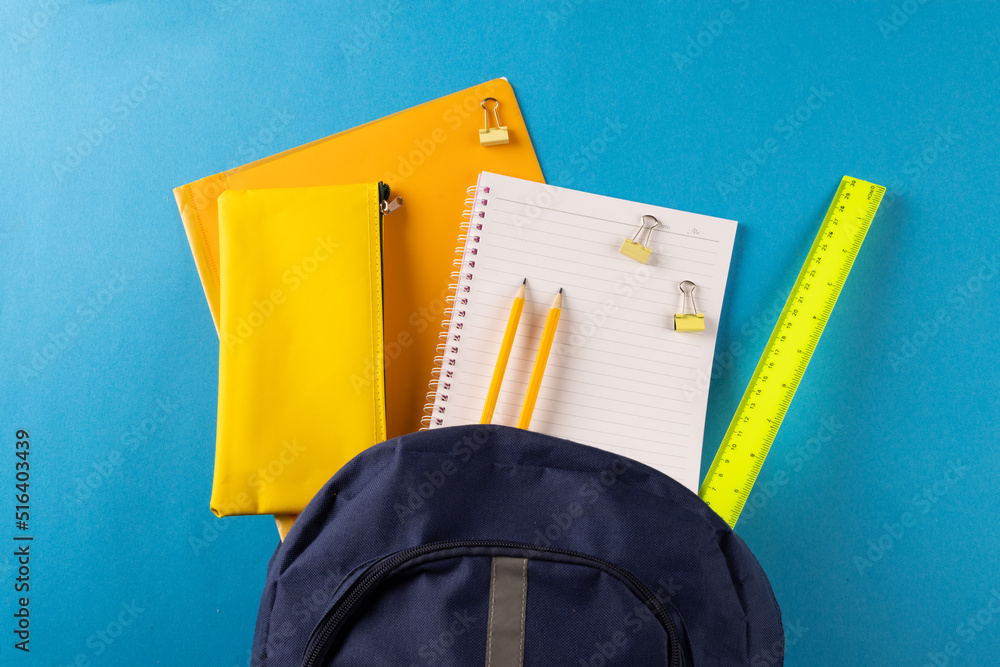 Image of school supplies, notebook, backpack, ruler, paper clips on blue background