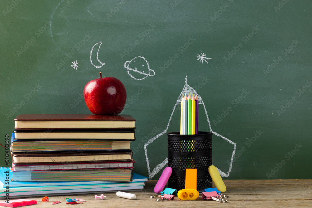 Image of school supplies, apple and notebook over drawings on black board