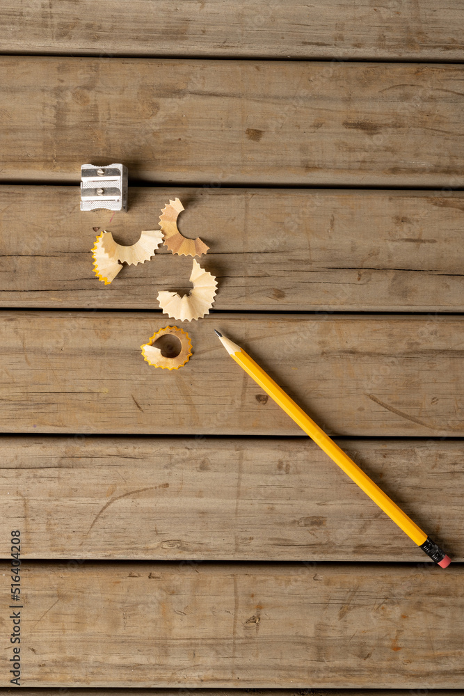 Vertical image of pencil, sharpener and peelings on wooden background