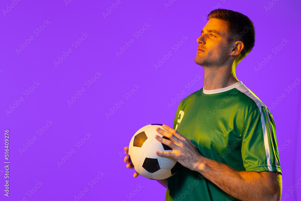 Caucasian male soccer player with football over neon pink lighting