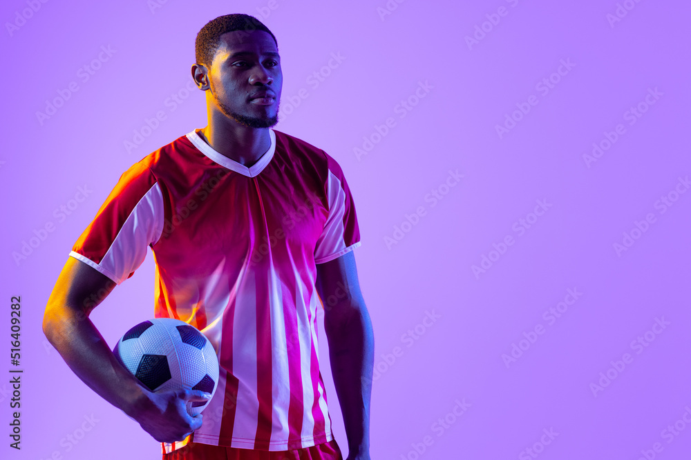 African american male soccer player with football over neon pink lighting