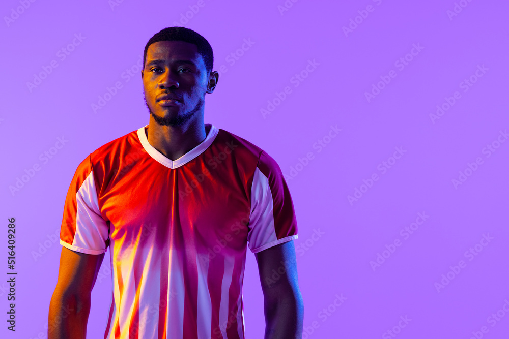 Portrait of african american male soccer player over neon pink lighting