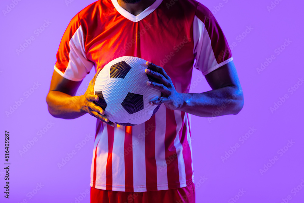 African american male soccer player with football over neon pink lighting