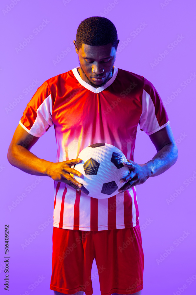 African american male soccer player with football over neon pink lighting