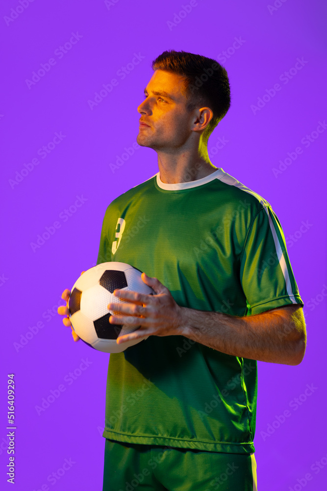 Caucasian male soccer player with football over neon pink lighting