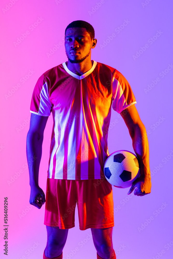 African american male soccer player with football over neon pink lighting