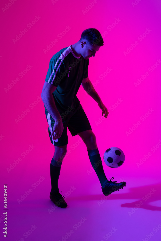 Caucasian male soccer player kicking football over neon pink lighting