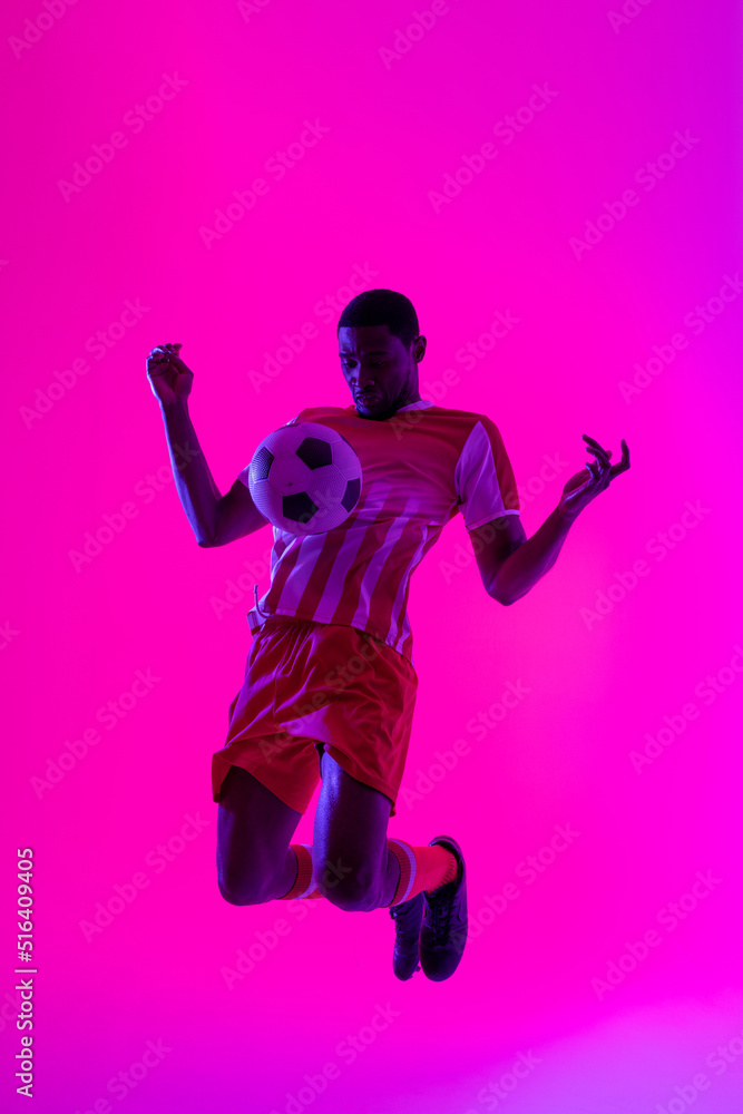 African american male soccer player with football over neon pink lighting