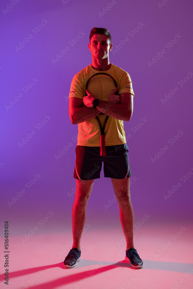 Portrait of caucasian male tennis player with tennis racket over neon pink lighting