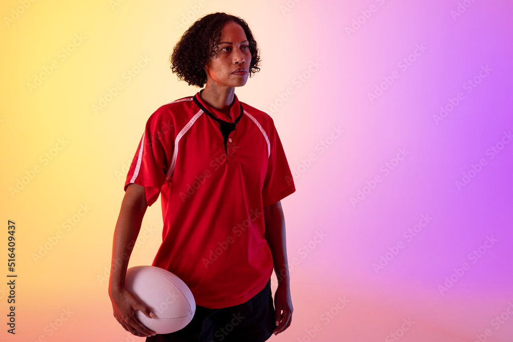 African american female rugby player with rugby ball over neon pink lighting