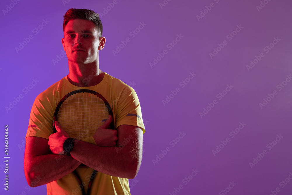 Portrait of caucasian male tennis player with tennis racket over neon pink lighting